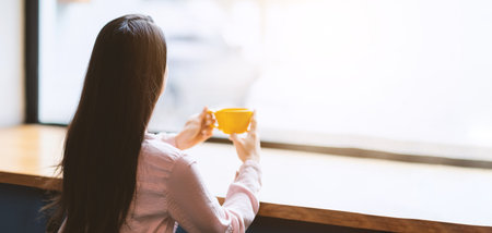 Unrecognizable young woman sitting in cafe and looking to outside the window, enjoying morning coffeeの写真素材