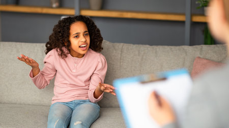 Psychological help. Emotional black teen girl talking to psychologist at her office, expressing emotionsの写真素材