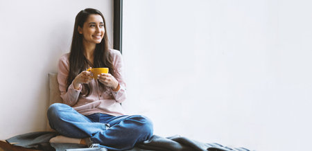 Happy latin woman enjoying coffee at cafe, sitting near window and looking into it, empty spaceの写真素材