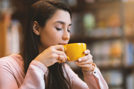 Time for coffee. Carefree arab lady sitting at cafe, holding mug of hot drink and enjoying aroma of...