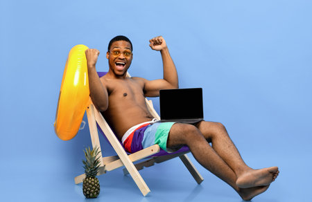 Black man showing laptop with empty screen while relaxing in lounge chair, gesturing YES on blue background, mockupの写真素材