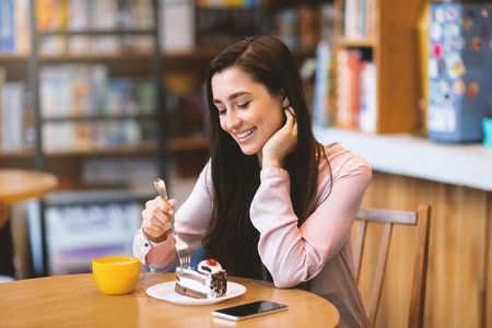 Positive lady enjoying cake and drinking coffee while sitting in cafe, spending time in cafeteria, copy spaceの写真素材
