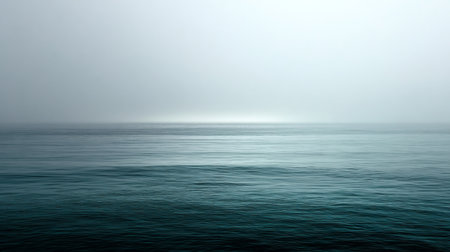 Gentle waves reflect soft hues of blue and grey in a serene, foggy morning atmosphereの素材