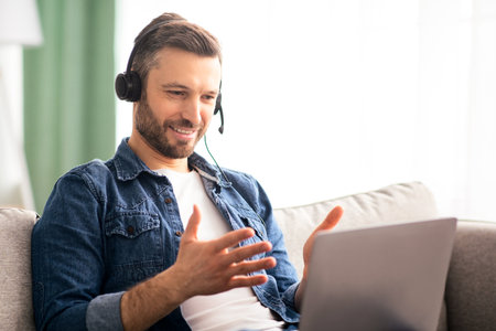 Positive man having video conference, using headset and laptop