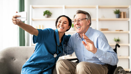 Happy disabled senior man in wheelchair and his nurse taking selfie together at homeの写真素材