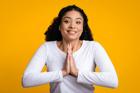 Cheerful young black woman pleading and asking for something with clasped handsの写真素材