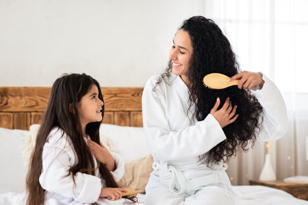 Fair-haired brunette mother and little daughter brushing hairの写真素材