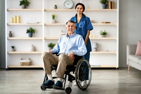 Full length portrait of older disabled man in wheelchair and his young caregiver smiling at camera in retirement homeの写真素材