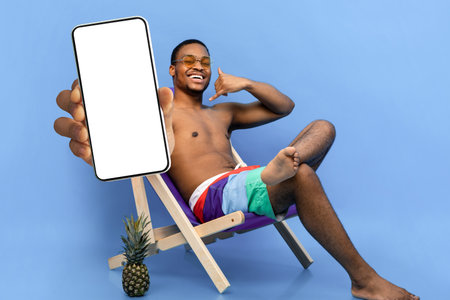 Flirty African American guy in swimwear showing CALL ME gesture, pointing at camera, sitting in...