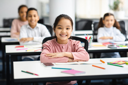 Portrait of small blackasian girl sitting at desk in classroomの写真素材