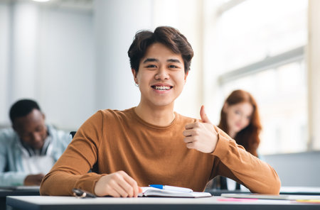 Asian male student sitting at desk showing thumbs up gestureの写真素材