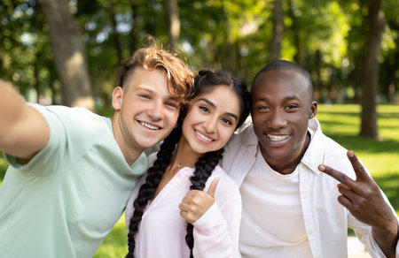 Multiracial students friends making selfie, gesturing v-sign and showing thumb up, posing outdoors...