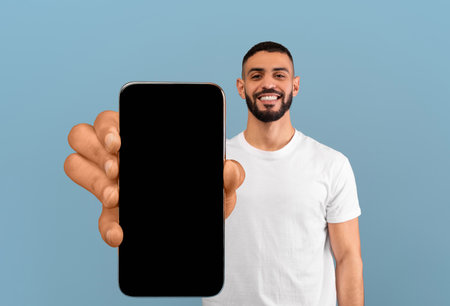 Cheerful young middle eastern man holding smartphone with empty screen