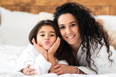 Adorable mother and daughter in bathrobes laying on bedの写真素材
