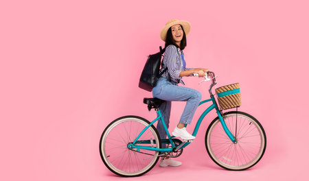 Excited asian woman riding retro bicycle with wicker basketの写真素材