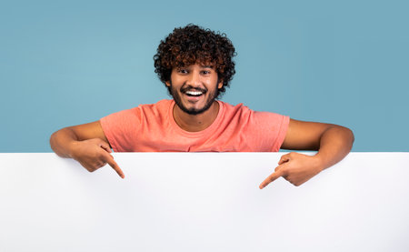Smiling young hindu man pointing down at blank advertising boardの写真素材
