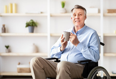 Positive senior impaired man in wheelchair drinking coffee or tea at homeの写真素材