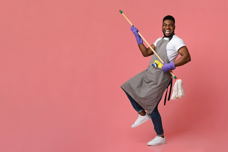Funny African Man Using Mop Handle As Guitar, Having Fun During Cleaningの写真素材