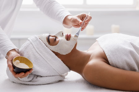 Therapist applying clay face mask on black girl, spa interiorの写真素材