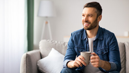 Cheerful bearded man enjoying cup of coffee at homeの写真素材