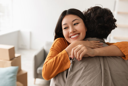 Smiling young Asian woman hugging her boyfriend and holding house key on moving day, free spaceの写真素材