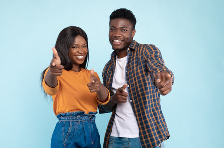 Happy black couple pointing fingers at camera at studioの写真素材