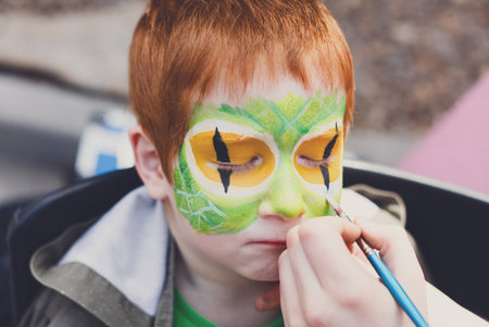 Child face painting process at redhead boy