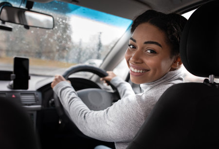 Woman in indoor car keeps wheel, turning around, talking with client passenger in back seatの写真素材