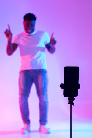 Black male influencer shooting video for social media on mobile phone, having fun in neon light, mockupの写真素材