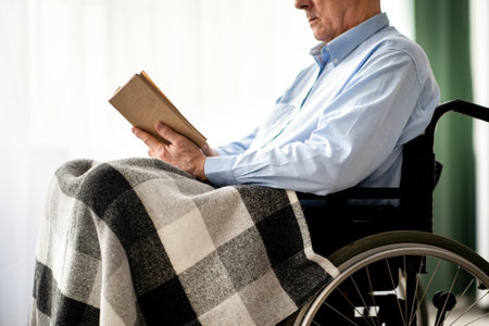 Cropped view of senior disabled man in wheelchair reading book indoorsの写真素材