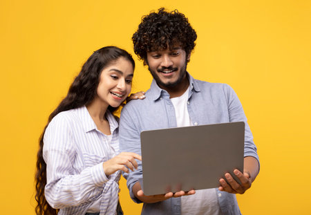Online education, remote work and shopping. Happy indian couple looking at laptop, choosing purchase or watching lessonの写真素材