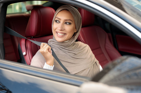 Smiling Muslim Lady In Hijab Putting On Seat Beltの写真素材