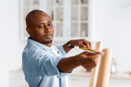 African american handyman working at home, measuring the width between legs of wooden table, assembling furnitureの写真素材