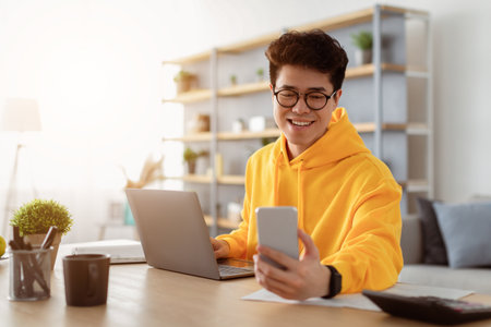 Happy asian man sitting at desk reading text message