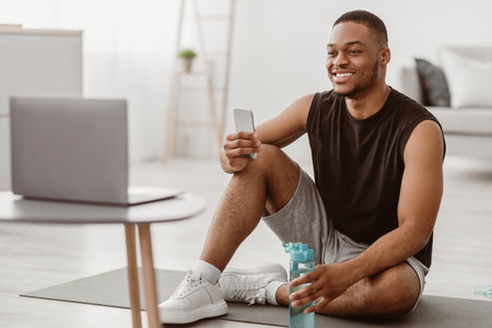 African Guy Holding Smartphone Watching Online Training On Laptop Indoorsの写真素材
