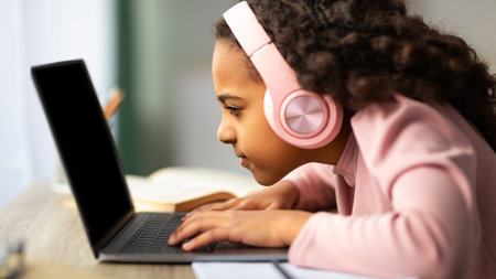 Youth and technology concept. Focused black schoolgirl using laptop computer, sitting at table too...
