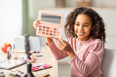 Beauty blog. Black teenage girl doing makeup and recording vlog on phoneの写真素材