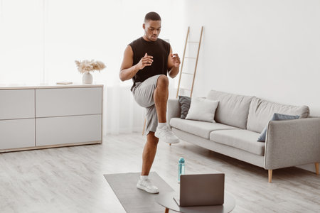 Black Man Doing Standing Knee Raise Exercise At Laptop Indoorの写真素材