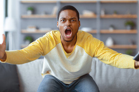Furious black guy watching football game on TVの写真素材