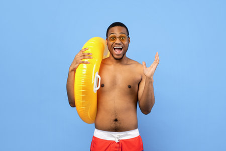 Emotional black guy in swimwear holding inflatable ring, shouting WOW, having great summer vacation,...