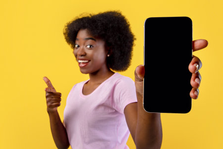 Mockup for application screen or text. African american woman showing blank mobile phone screen, yellow backgroundの写真素材