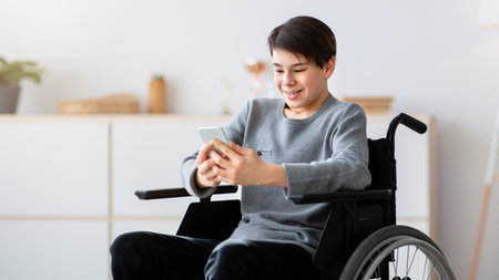 Happy disabled teen in wheelchair using digital tablet at home, browsing internet or watching...