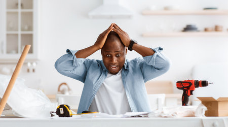 Frightened handyman having problems in assembling new furniture, sitting in kitchen interiorの写真素材
