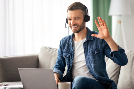 Smiling man having business video conference, using headset and laptop