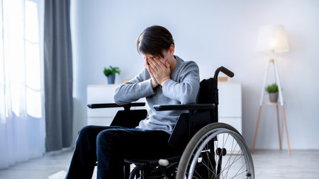 Depression in disabled teenagers. Unhappy handicapped teen boy in wheelchair crying at homeの写真素材