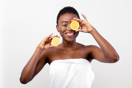 Excited african american lady with lemon halves in hands, posing wrapped in towel over blue backgroundの写真素材