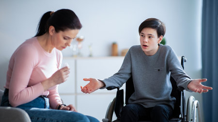 Family disagreement. Upset mother crying and her teenage son in wheelchair trying to justify himself at homeの写真素材