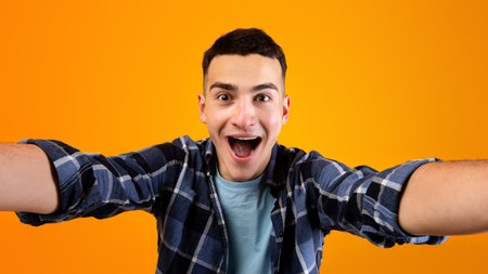 Happy millennial guy taking selfie on orange studio backgroundの写真素材