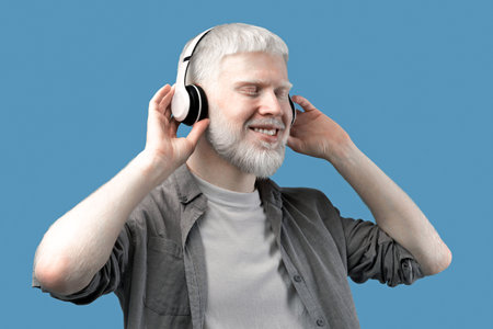 Happy albino man in headphones listening to music, enjoying his favorite song on turquoise studio...