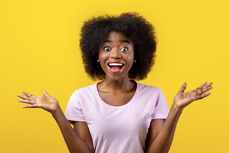 Omg. Overjoyed african american lady shouting in excitement and looking at camera, posing over yellow studio backgroundの写真素材